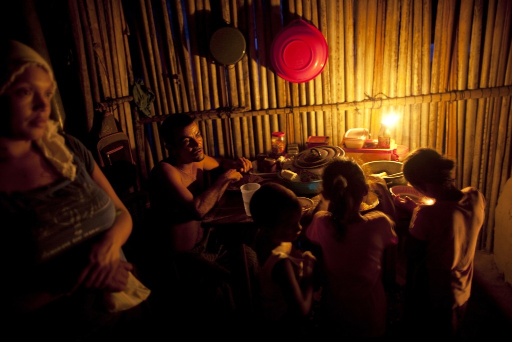 In this May 5, 2012 photo, a family eats dinner lit by candlelight in "La Confianza" peasant model city, Bajo Aguan, Honduras. Peasants from MUCA (Movimiento Unificado Campesino del Bajo Aguan) occupied around 7000 sq meters of productive land close to the city of Tocoa in the Valley of Bajo Aguan, eastern coast of Honduras in December, 2009. They operate a comercial production of african palm and they also stablished what they call a "peasant model city" called "La Confianza" where more than 300 hundred families live. Since then an open conflict between them and the alleged owner of the land, Miguel Facussé, one of the most powerful businessmen in Honduras has left more than 60 people dead including peasants, security guards, a journalist and members of the Honduran national police. (AP Photo/Rodrigo Abd)