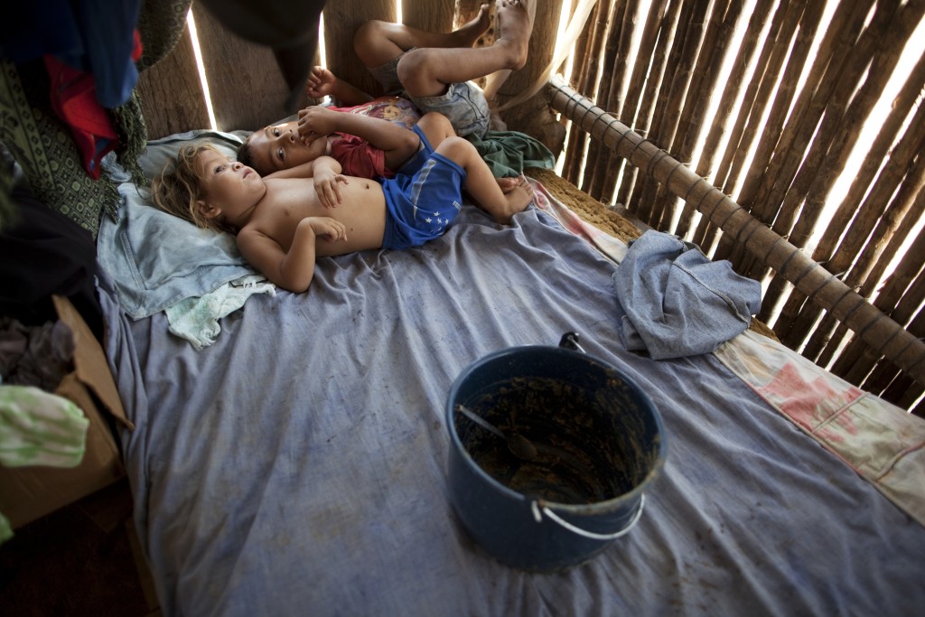 In this May 5, 2012 photo, Gerson Sarai Melgar, 3, blue shorts, and his brother Edwin Isidro Melgar, 6, rest after eating from a pot inside their house in "La Confianza" peasant model city, Bajo Aguan, Honduras. Peasants from MUCA (Movimiento Unificado Campesino del Bajo Aguan) occupied around 7000 sq meters of productive land close to the city of Tocoa in the Valley of Bajo Aguan, eastern coast of Honduras in December, 2009. They operate a comercial production of african palm and they also stablished what they call a "peasant model city" called "La Confianza" where more than 300 hundred families live. Since then an open conflict between them and the alleged owner of the land, Miguel Facussé, one of the most powerful businessmen in Honduras has left more than 60 people dead including peasants, security guards, a journalist and members of the Honduran national police. (AP Photo/Rodrigo Abd)