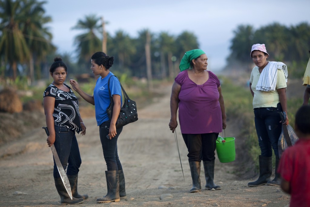 In this May 7, 2012 photo, women wait for a truck to carry them to work in an african palm tree plantation in "La Confianza" peasant model city, Bajo Aguan, Honduras. Peasants from MUCA (Movimiento Unificado Campesino del Bajo Aguan) occupied around 7000 sq meters of productive land close to the city of Tocoa in the Valley of Bajo Aguan, eastern coast of Honduras in December, 2009. They operate a comercial production of african palm and they also stablished what they call a "peasant model city" called "La Confianza" where more than 300 hundred families live. Since then an open conflict between them and the alleged owner of the land, Miguel Facussé, one of the most powerful businessmen in Honduras has left more than 60 people dead including peasants, security guards, a journalist and members of the Honduran national police. (AP Photo/Rodrigo Abd)